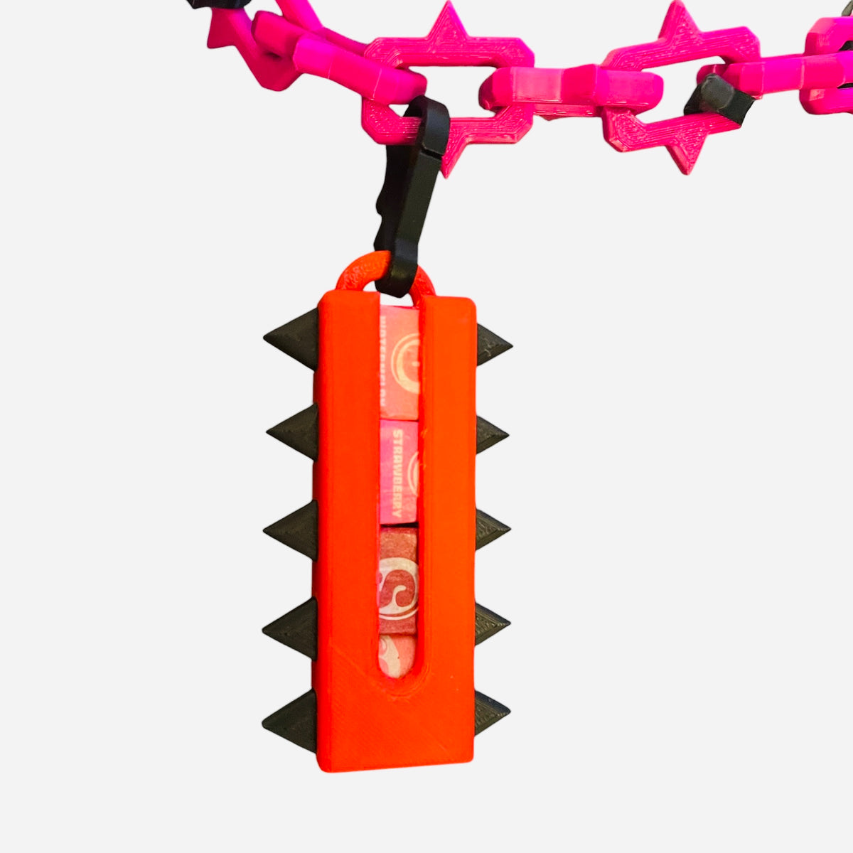 A red candy holder with black spikes, hanging from a hot pink chain, on a white background.