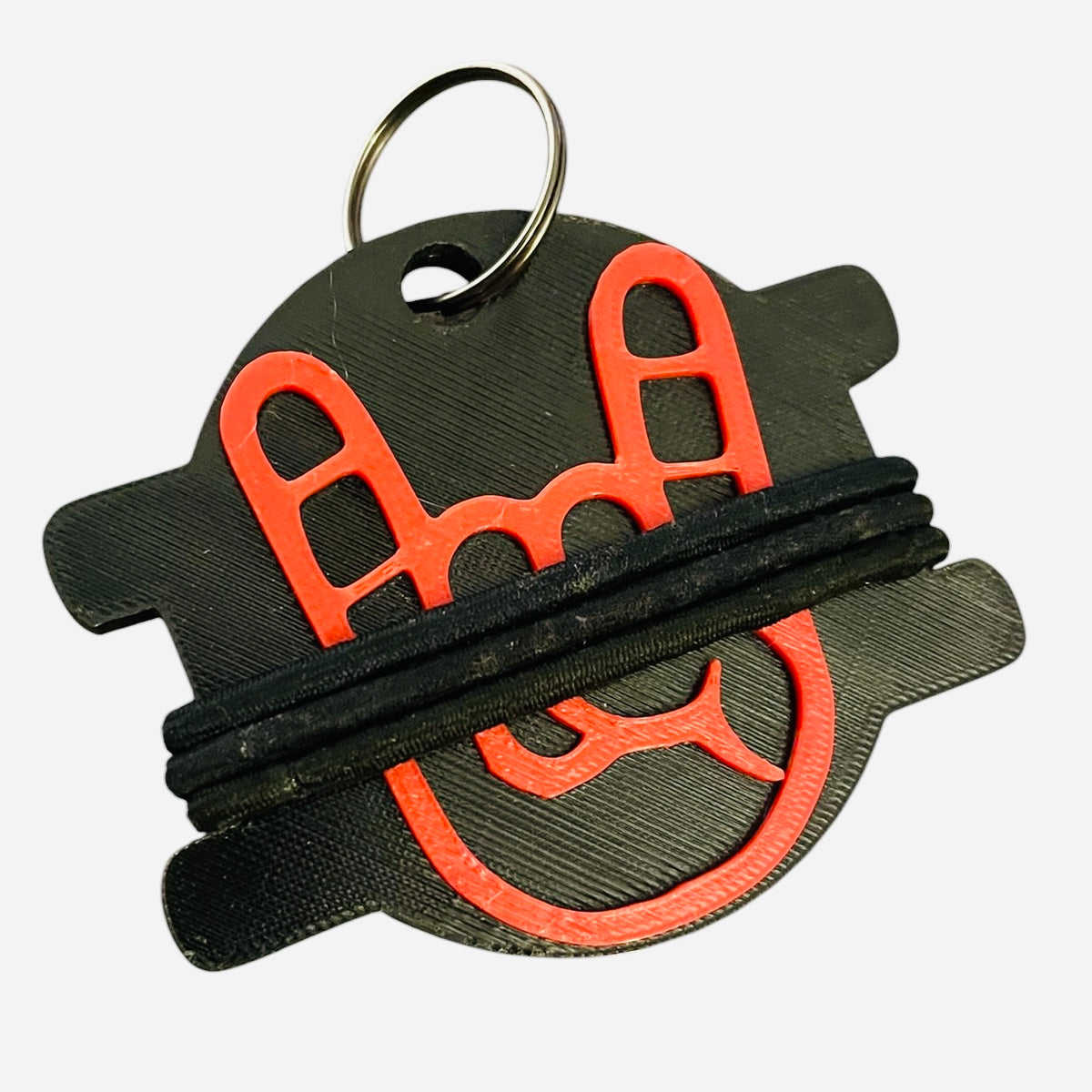 A 3D-printed keychain charm featuring a black rock on hand design with a red emblem and three wrapped black elastic bands, attached to a metal keyring.
