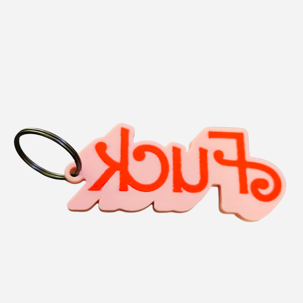 A pink and red keychain featuring stylized barbie script that reads 'FUCK' upside down, attached to a black metal split ring, shown on a white background.