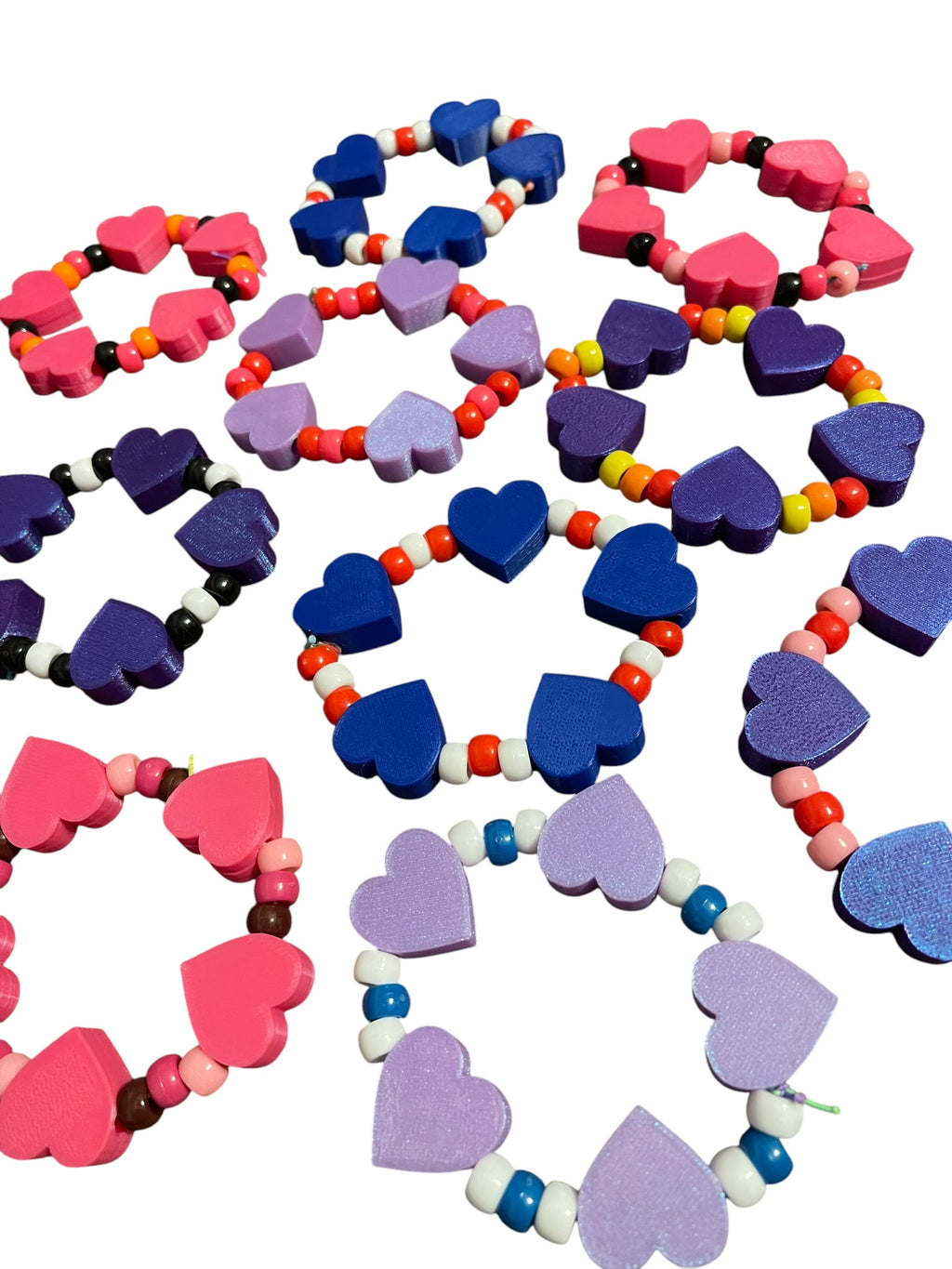 A collection of 3d printed heart beaded bracelets in various colors including pink, purple, blue, orange, yellow, and white, arranged on a plain white background.