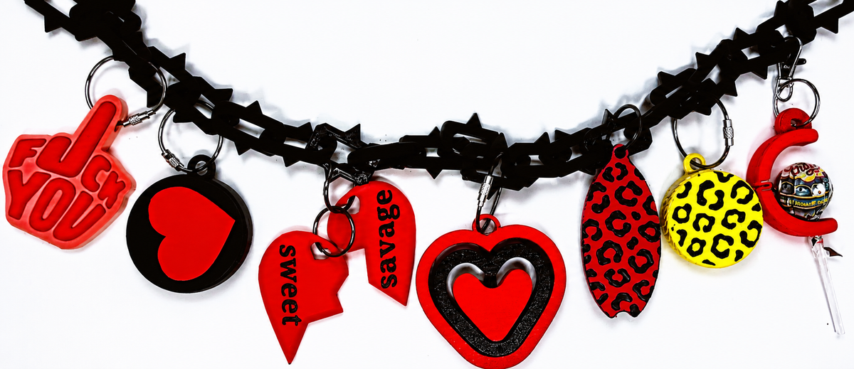 A black studded bag chain with multiple red, black, yellow, and leopard-print heart and container charms, shown against a plain white background.