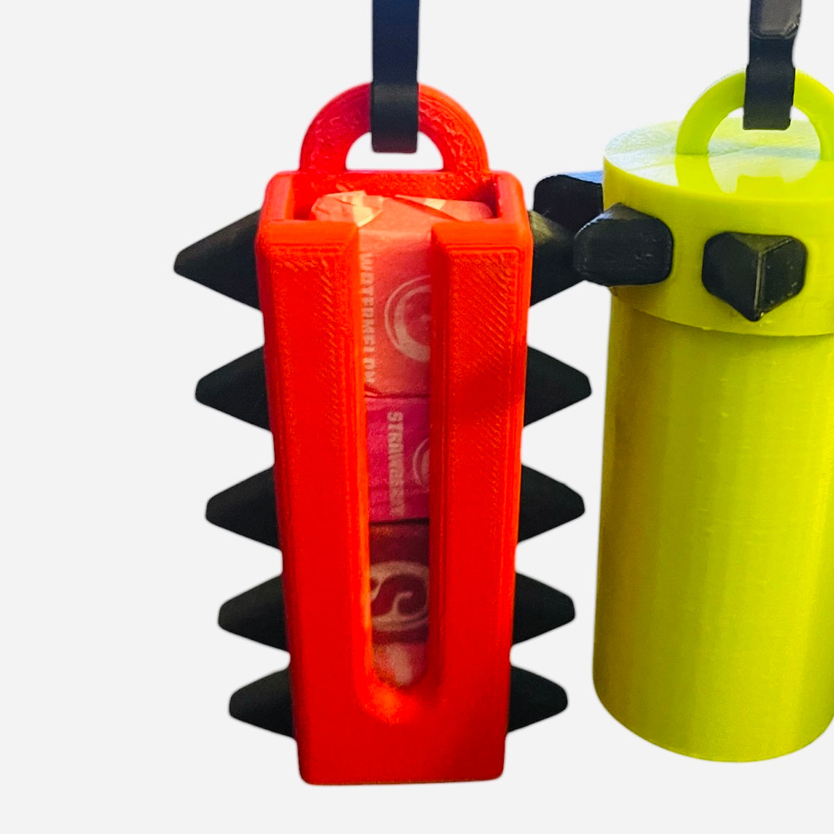 A close-up of a bright red 3D-printed hanging organizer holding pink packaged items, with a second lime green cylindrical holder partially visible beside it on a plain light background.