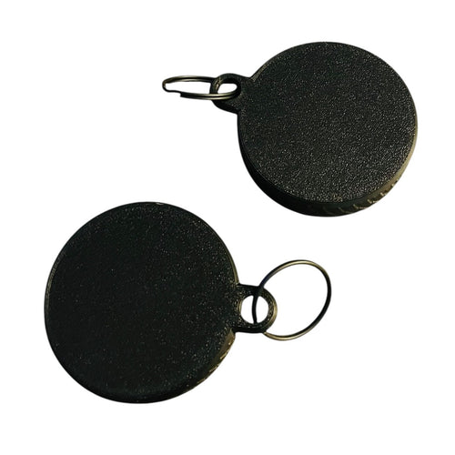 The backs of two round black screw top container keychains on a white background. Both feature a black split ring.