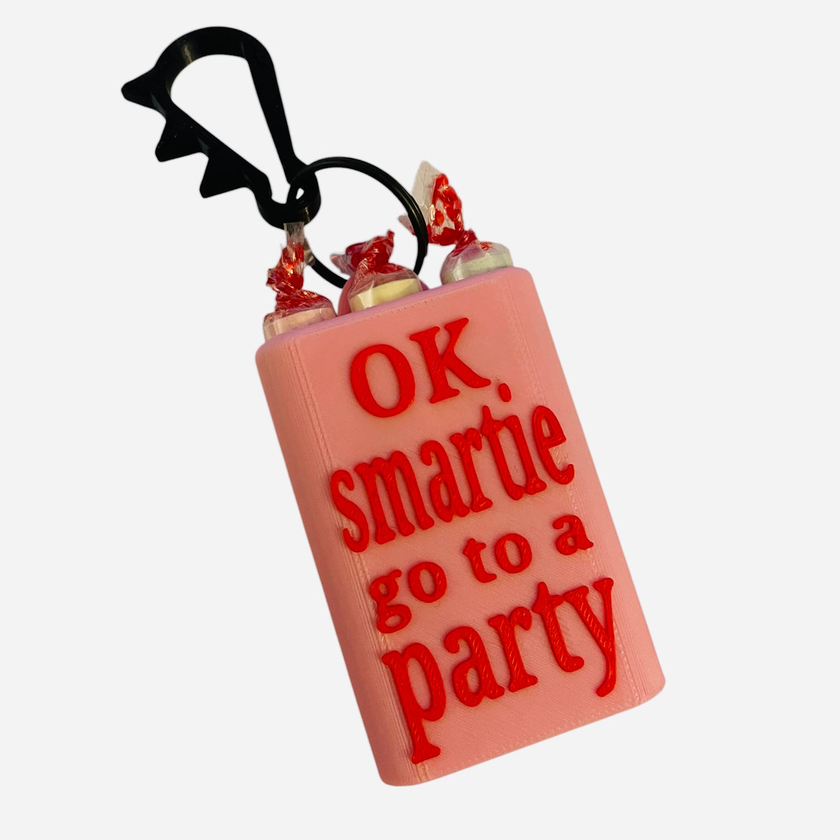A novelty keychain or bag charm candy holder with red text reading 'OK, smartie go to a party' and a black carabiner clip, shown on a white background.