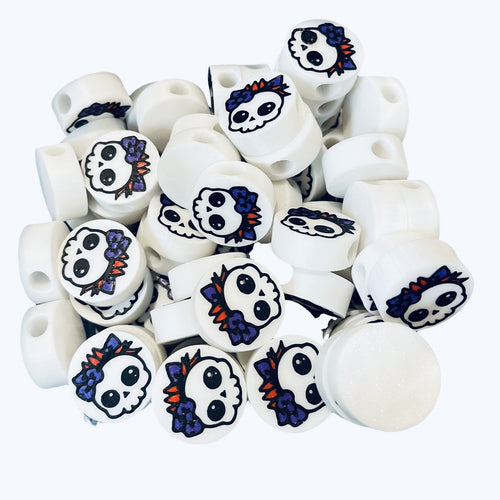 White round beads with a girly skull design with red hair and a blue bow. 